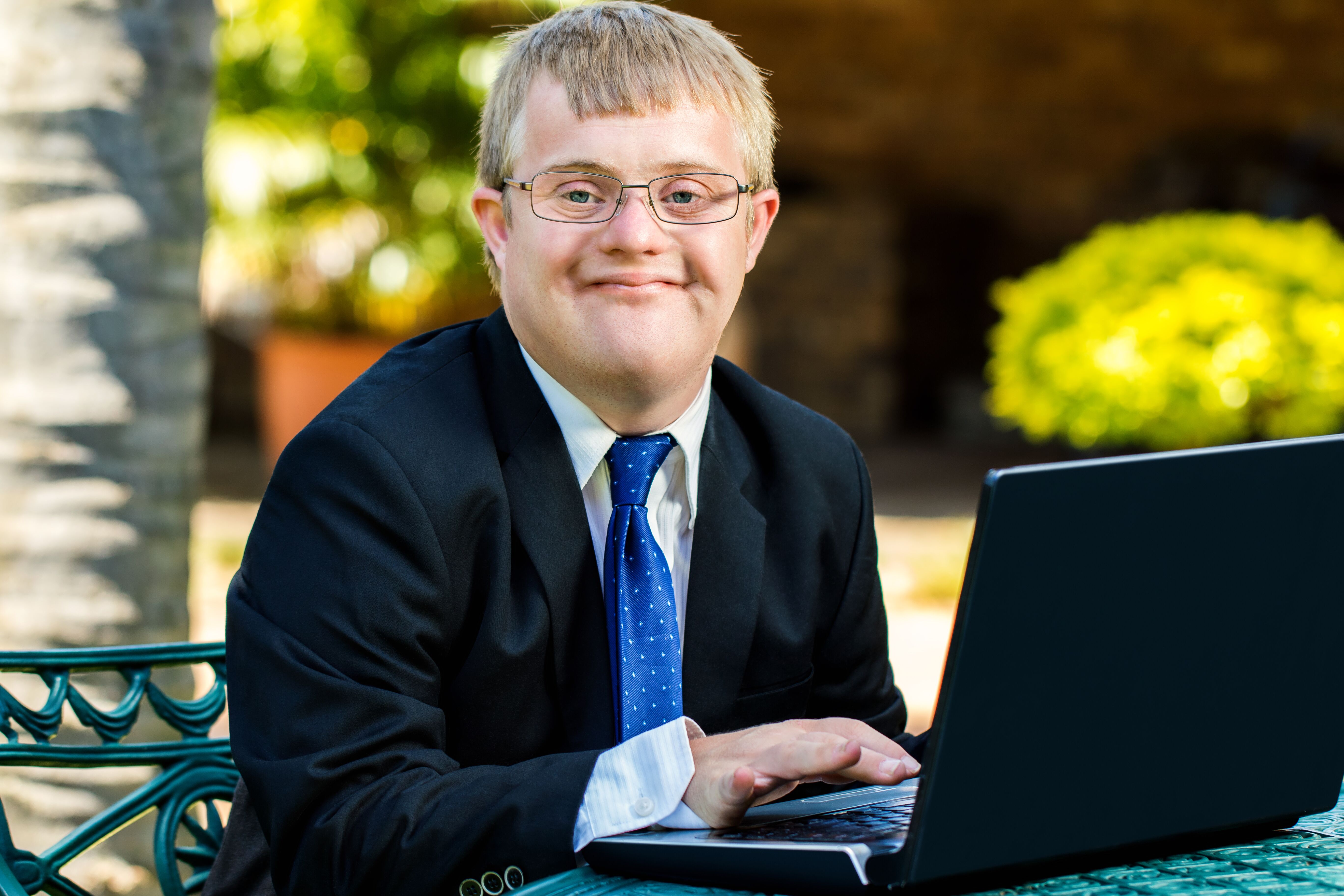 Boy with Down syndrome in suit jacket and tie, sitting behind a laptop and smiling